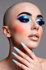 Bold blue eyeshadow and striking makeup on a confident bald woman with light blue nails, exuding modern beauty and creative expression