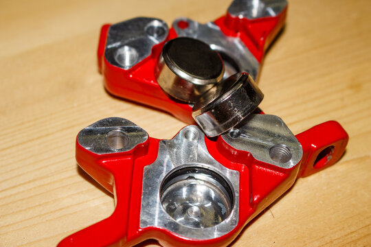 Red mountain bike hydraulic caliper components, disassembled for service. Pistons and internal parts visible for maintenance and repair on wood surface