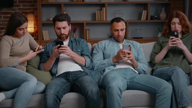 Focused four diverse friends overuse mobile phones addiction internet social media dependence relaxing at home boring party looking in smartphones addicted multiethnic men women ignoring each other