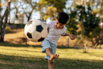 Obraz premium Excited boy kicking soccer ball outdoors on a sunny day