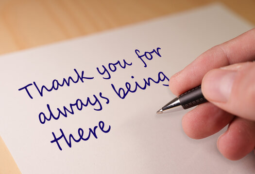 Hand writing a personal thank you message on a white card with blue ink, conveying appreciation, friendship, and support to someone for always being present