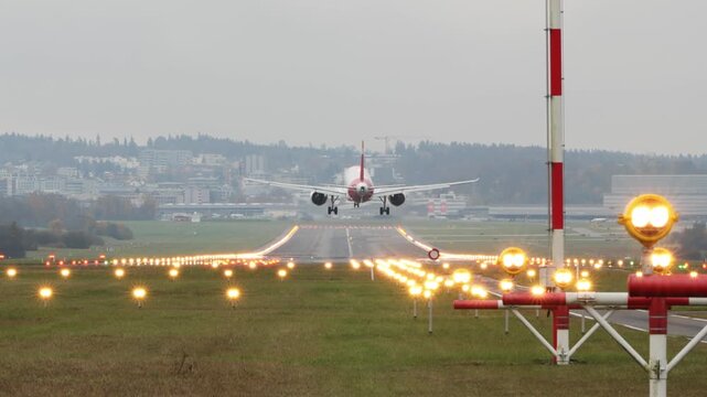Rear long shot footage of a commercial passenger plane moments before touchdown. Real time, super telephoto footage, foggy autumn weather, illuminated runway, international flight, European Airport 