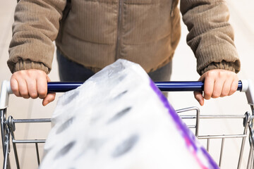 A person in a winter jacket pushes a shopping cart carrying a large package of toilet paper,suggesting panic buying or stocking up