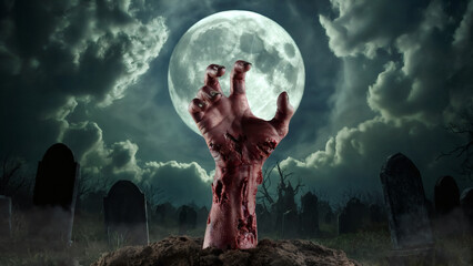 Terrifying zombie hand emerges from grave under eerie full moon in spooky graveyard