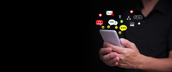 Person using smartphone with floating chat icons, emojis, and social media symbols with copyspace on dark background, representing online communication, messaging, and digital connection.