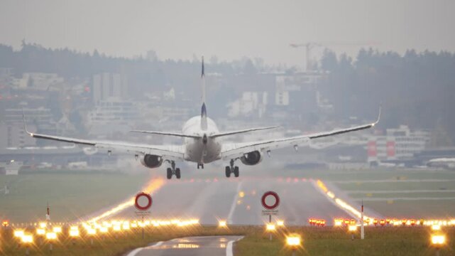 Rear long shot footage of a commercial passenger plane moments before touchdown. Real time, super telephoto footage, foggy autumn weather, illuminated runway, international flight, European Airport 