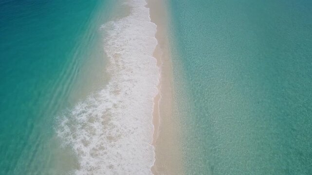 Breathtaking aerial view captures the serene separation of vibrant turquoise ocean waters by a pristine sandy beach, with gentle white waves caressing the shore