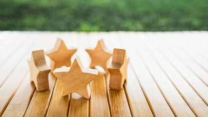 Wooden stars standing on wooden floor with green grass background. Concept of five-star rating, quality, excellence, customer satisfaction, business review, leadership, and success.