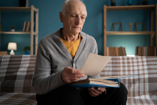elderly man looking old photo sitting on sofa at home. Retirement problem concept