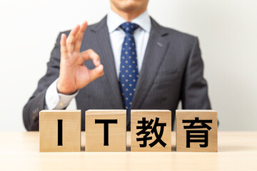 「IT教育」と書かれたブロックとOKポーズをするビジネスマン