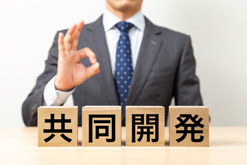 「共同開発」と書かれたブロックとOKポーズをするビジネスマン