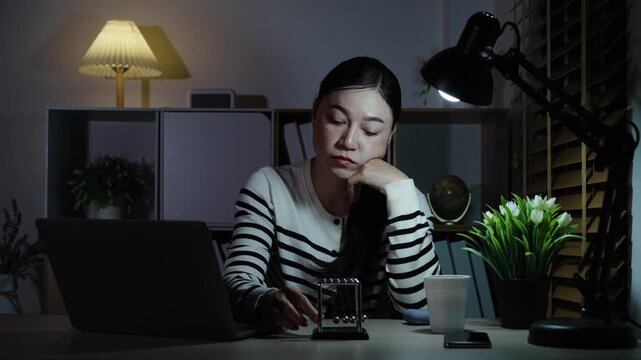 bored woman working with laptop and staring at Netwon's cradle balls swinging at a night