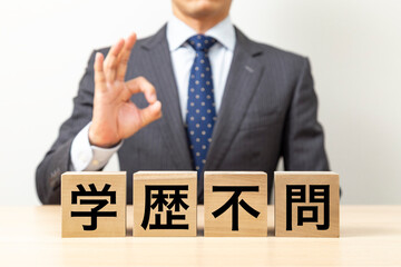 「学歴不問」と書かれたブロックとOKポーズをするビジネスマン