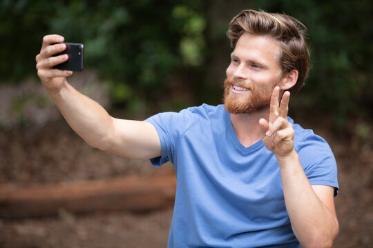 man makes selfie in forest making victory sign