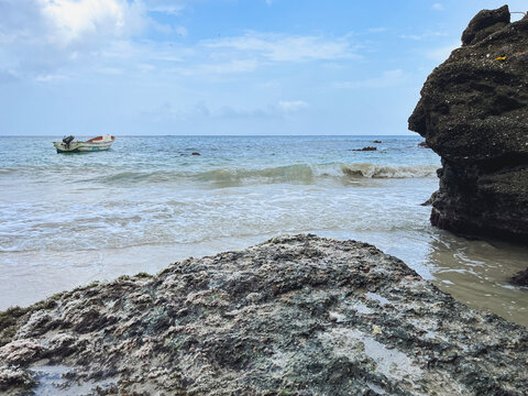 Tropical seascape with a rocky shore and a small fishing boat under a blue sky - Powered by Adobe