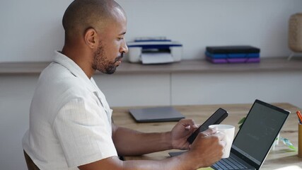 Video of businessman working with statistics on his laptop while using his phone in the office - Powered by Adobe