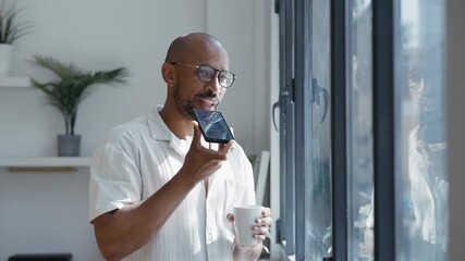 Video of businessman sending audios with smartphone while standing near the window in the office - Powered by Adobe