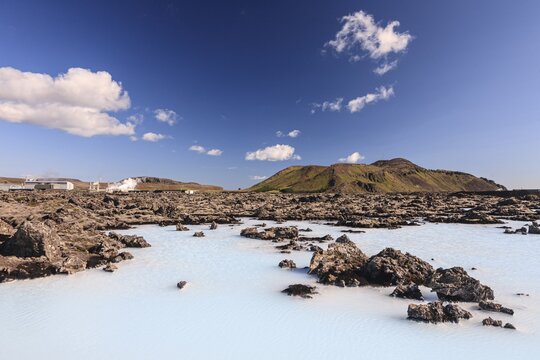 Outdoor thermal pool and geothermal power plant in front of volcanic mountains, Blue Lagoon, summer, sunny, Grindavik, Reykjanes, Iceland