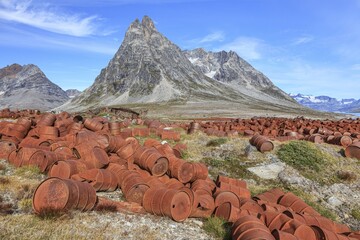 Rusted oil barrels on a fjord in front of steep mountains, remains of a US airbase from the Second World War, Ikateq Fjord, East Greenland, Greenland