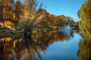 Serene autumn park scene with tranquil lake, colorful foliage, and gentle fountain spray