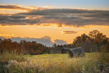 Obraz premium Scenic autumn landscape with hay bales under a colorful sunset sky and vibrant foliage