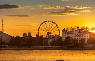 Sunset view of a city skyline with a large Ferris wheel and calm water reflections