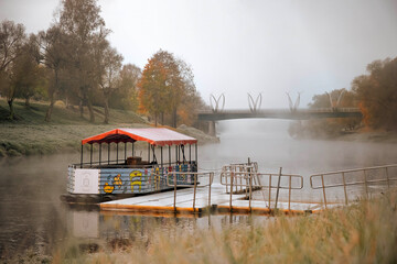 Colorful boat docked on a misty riverbank with trees and bridge in the background