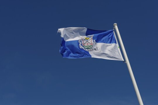 Close-up of a blue and white flag of the Capalas region in the wind on a flagpole against a bright blue sky, Capelas, Sao Miguel Island, Azores, Portugal
