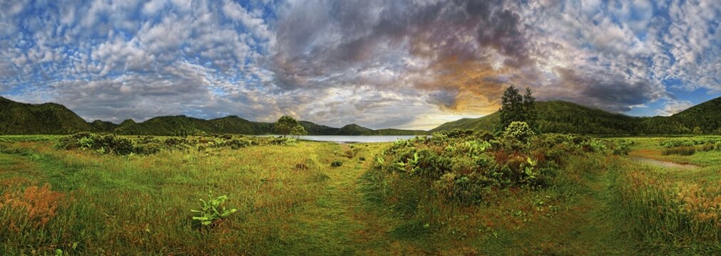 360&deg; panorama with a meadow and mountains in the background, a lake in the distance, dramatic sky at sunset, crater lake Lagoa do Fogo, Caldeiras, Sao Miguel Island, Azores, Portugal