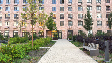 Modern residential building with patterned pink facade, landscaped courtyard, benches, and young trees, representing urban architecture, comfort, and sustainable city living concepts