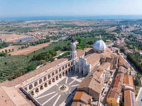 Aerial view of the Basilica della Santa Casa's dome gleaming under the sun, terracotta roofs sprawling towards the Adriatic, a tapestry of history and faith, Loreto, Ancona, Italy.