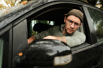 Man leaning from car window adjusting side mirror on rainy day. Concept of safety, driving, and readiness