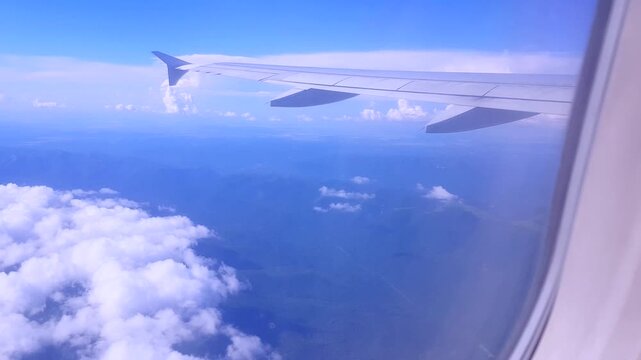 Flying above mountains and clouds through the plane window camera movement clear sky and soft blue gradient versatile background for titles mapping aviation and inspiring clips