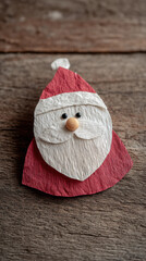 Handmade santa craft made from textured paper with simple facial details, cute kids christmas diy project placed on rustic wooden surface