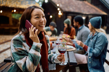 Happy Korean woman talking on cell phone during lunch party with friends on patio.