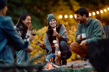Happy friends having fun while roasting marshmallows in backyard.