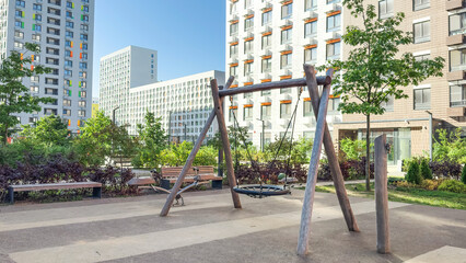 Fototapeta premium Urban playground with wooden swing and benches surrounded by modern residential buildings and greenery, symbolizing safe outdoor spaces and community lifestyle in contemporary city environments