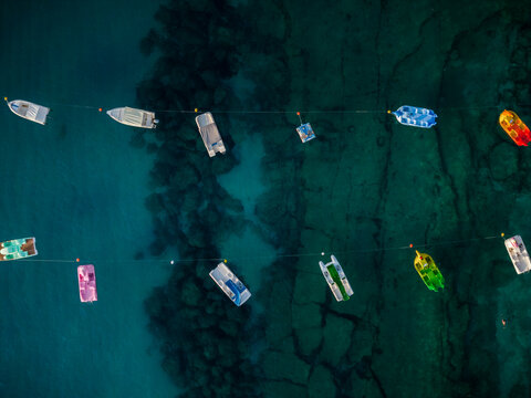 Aerial view of boats floating on the turquoise water, with colorful hues reflecting on the surface, casting shadows on the seabed, Tropea, Calabria, Italy.