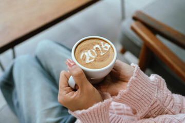A person holding a cup of coffee with latte art showing the number 