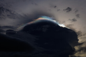 A dramatic dusk sky shows a towering dark storm cloud with a subtle rainbow halo along its edge, creating contrast between shadow and light and evoking awe and natural wonder.