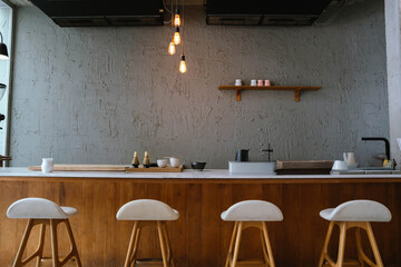 Modern minimalist kitchen interior with wooden counter, bar stools, warm lighting, and simple decor creating a cozy and stylish atmosphere.