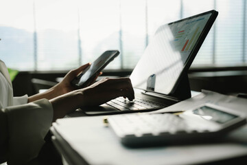 Obraz premium A person working with a calculator and financial documents on a desk, analyzing data from charts displayed on a laptop in a bright office environment.