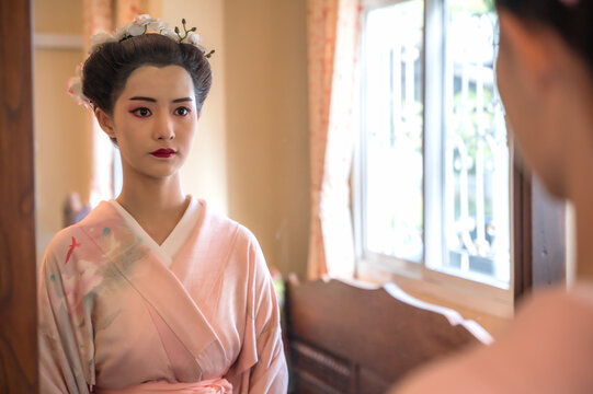 Young pretty Japanese woman in elegant traditional kimono or yukata looking at herself in mirror
