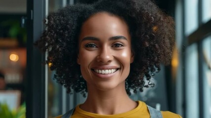A smiling woman with curly hair stands in a brightly lit shop, wearing an apron, embodying small business success and warmth.