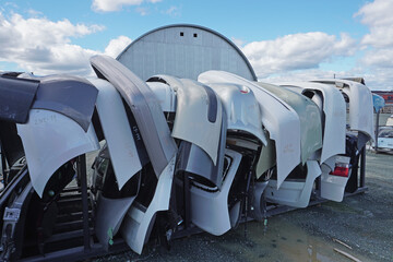 A row of car bumpers on metal racks under the open sky. Body panels for disassembly, hangar on the...