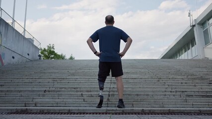 Male athlete with prosthetic leg standing at the bottom of outdoor stairs, preparing for a workout and running challenge, rear view. - Powered by Adobe