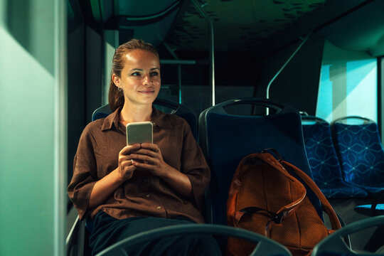 Female with smartphone traveling by city by at night.
