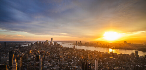Aerial panoramic view of New York City skyline at sunset with golden sunlight reflecting on the Hudson River and modern skyscrapers glowing in evening light