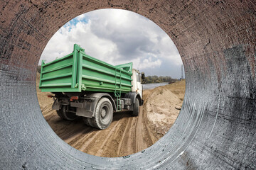 Heavy construction equipment is seen from a pipe, adding to the bustling activity on the site while clouds drift above in an open sky