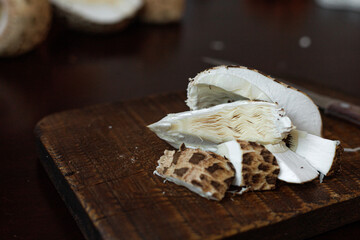 Sliced Macrolepiota procera, the parasol mushroom, on a dark wooden board with visible fibrous white flesh and brown patterned cap. Concept of organic food, texture study, culinary background.